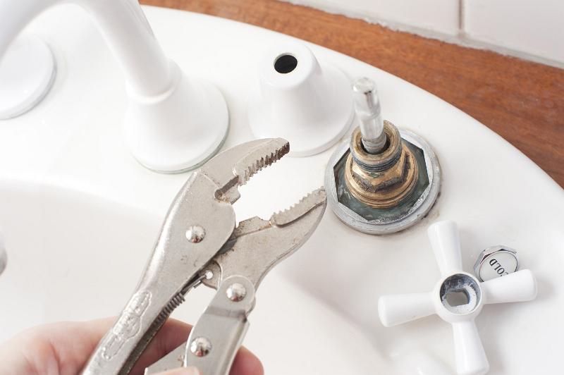Free Stock Photo: Man doing home plumbing maintenance fixing a faucet or tap on a sink with a mole grip wrench