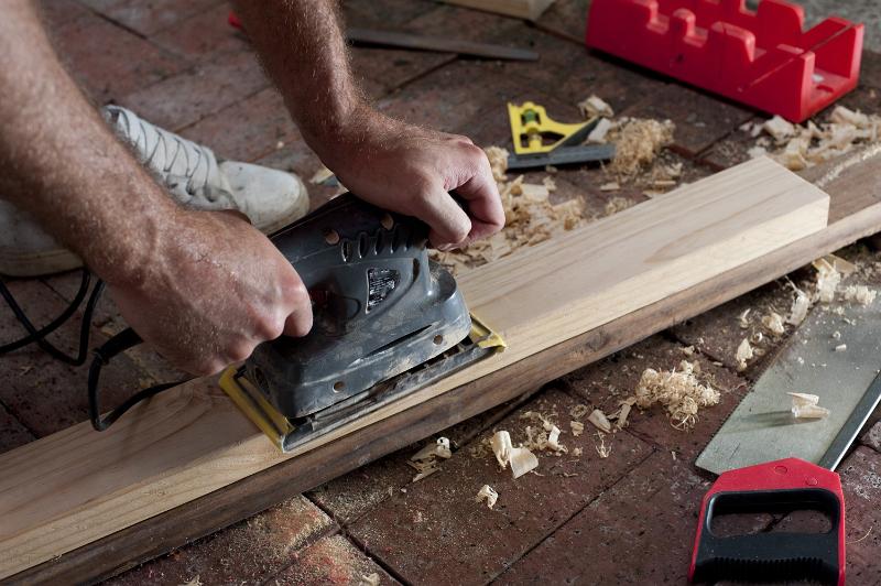 Free Stock Photo: Woodworker, carpenter or joiner sanding a plank of wood with an electric sander on a brick floor in a DIY concept