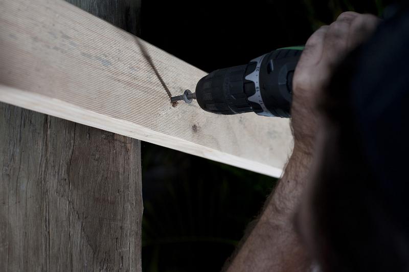 Free Stock Photo: Man fixing wood to a support with a screw using a screwdriver attachment on his electric drill, close up of his hand and the drill bit