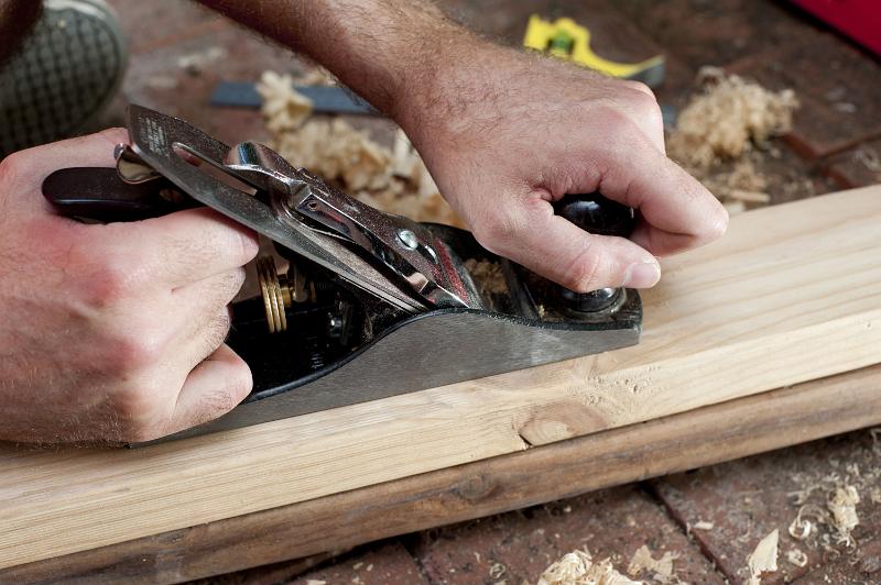 Free Stock Photo: Man planing a plank of wood with a handheld manual planer in a DIY, renovation and woodworking concept, close up view of his hands