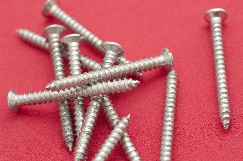 Free Stock Photo: Fully threaded silver metal woodworking screws piled randomly on a red background in a DIY concept, close up view from above