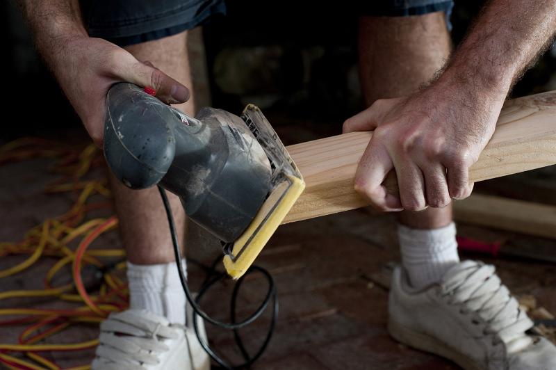Free Stock Photo: Handyman doing joinery using an electric sander to smooth the surface of a plank of wood before installing it in a house, close up of his hands