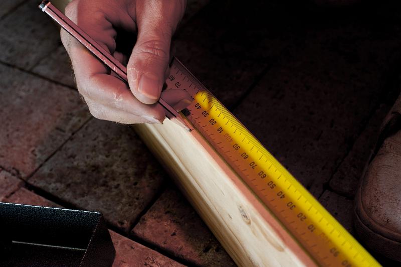 Free Stock Photo: Carpenter carefully measuring a length of wood with a tape measure repeating his measurement a second time for accuracy