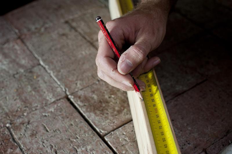 Free Stock Photo: Measuring the length of a plank of wood using a builders tape measure and pencil, close up of the carpenters hand