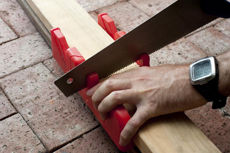 Free Stock Photo: Man using a mitre box with guides for specific angles of cut to saw wood on a brick floor in a DIY concept