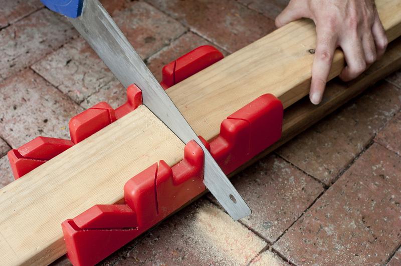 Free Stock Photo: Sawing wood with a mitre saw using a plastic guide to ensure a right angle with alternate slots for varying angles and degrees of cut, closeup of his hands and the tool