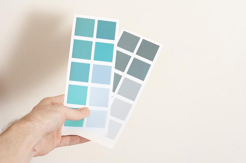 Man holding two cards with sample paint color swatches in grey and blue hues in his hand as he makes a decision on the interior decorating and renovation of his home