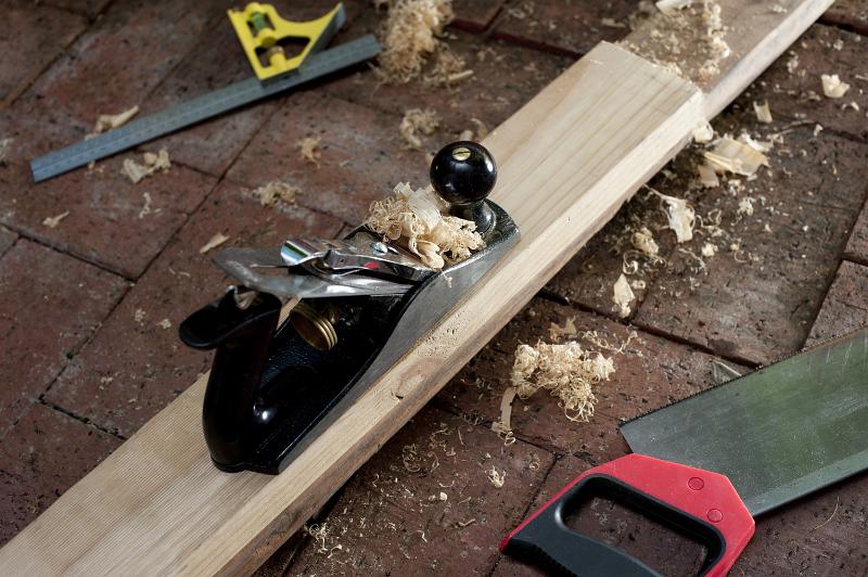 Free Stock Photo: Woodworking tools with a wood plane, tenon saw and right angle or metal ruler on a nrick floor with a half planed plank of wood