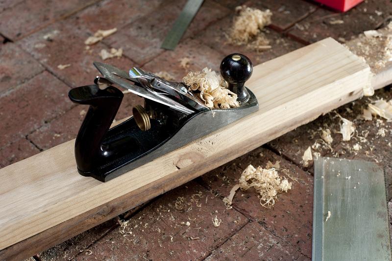 Free Stock Photo: Wood plane in a woodworking workshop resting on a half planed plank of wood surrounded by fresh wood shavings in a DIY and renovation concept