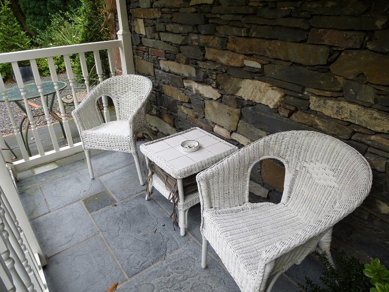 Free Stock Photo: White painted wicker table and armchairs on an outdoor patio or veranda enclosed by a railing on a stone house