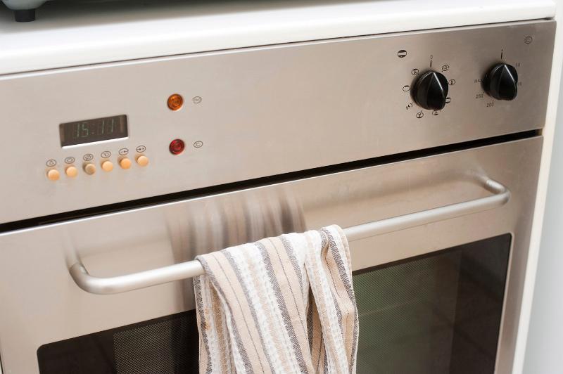 Free Stock Photo: Closeup of the front of an electrical domestic oven with an oven cloth draped over the hande of the door