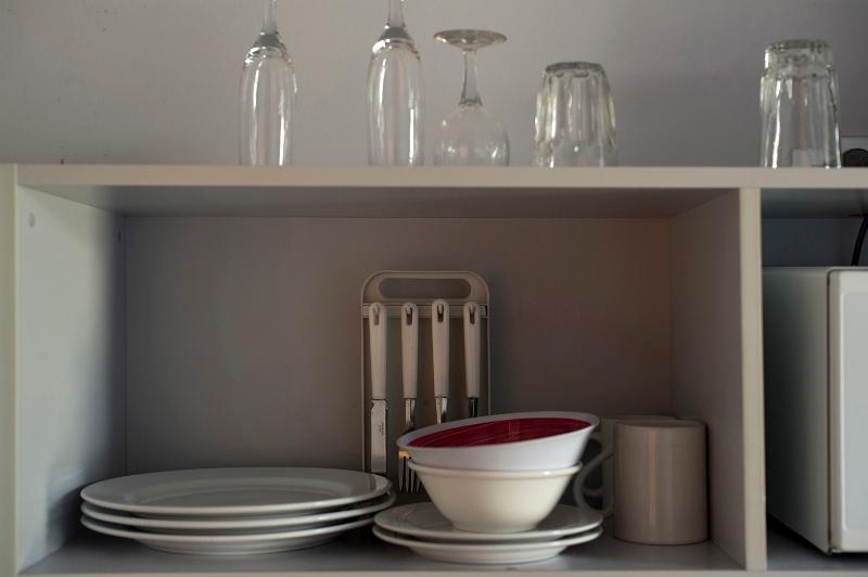 Free Stock Photo: A variety of ceramic plates, mugs and bowls on a kitchen shelf together with some glasses stored above