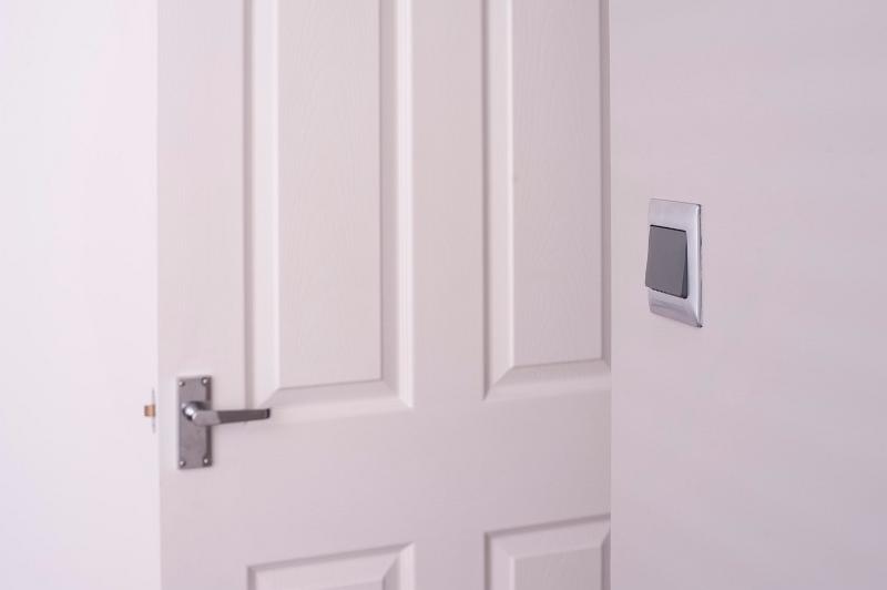 Free Stock Photo: Open white wooden paneled door with an electric light switch on the wall alongside it and a metal door handle