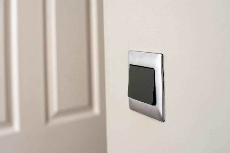 Free Stock Photo: Modern silver framed plastic light switch on a white wall alongside a white painted wooden paneled door