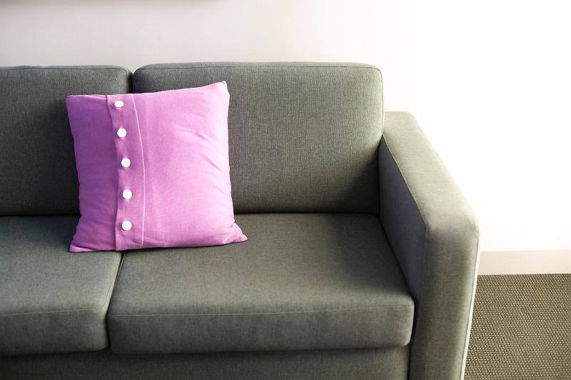 Free Stock Photo: Pink cushion on a comfortable upholstered grey sofa, close up view against a white wall with copyspace