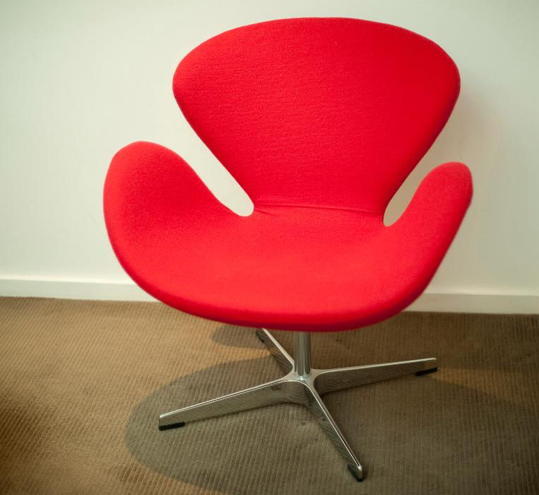 Free Stock Photo: Retro-style chair with a molded modular design in red and a steel base standing on a brown carpet against a white wall in an interior decor concept
