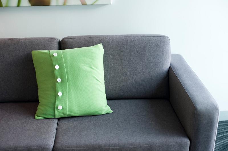 Free Stock Photo: Grey upholstered sofa with a green cushion with button detail, close up view