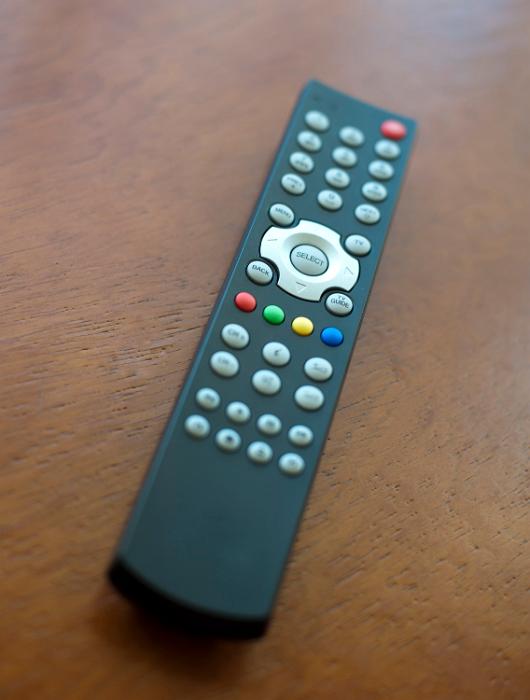 Free Stock Photo: Close up of an infrared television remote control lying on brown wood surface at an oblique angle