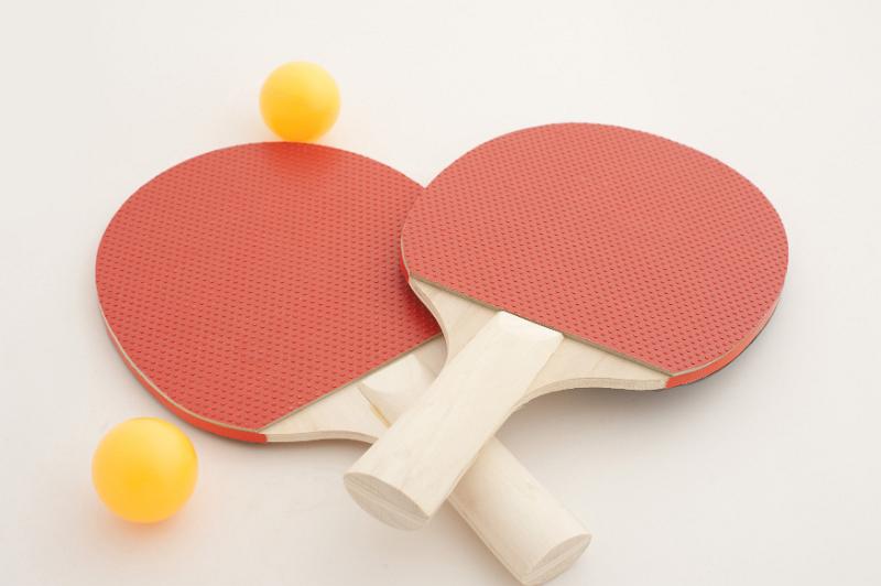 Free Stock Photo: Two colorful red wooden ping pong or table tennis bats lying crossed over on a white background with two loose yellow balls alongside