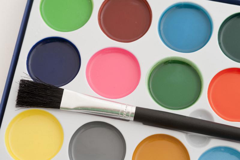Free Stock Photo: New open box of kids watercolor paints with round pots of paint and a brand new unused paintbrush viewed close up from above