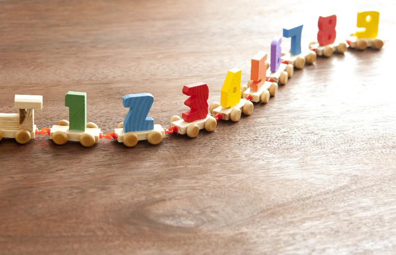 Free Stock Photo: Still Life of Long Wooden Toy Train Towing Colorful Counting Cars with Numbers One Through Nine on Wooden Floor Surface with Copy Space