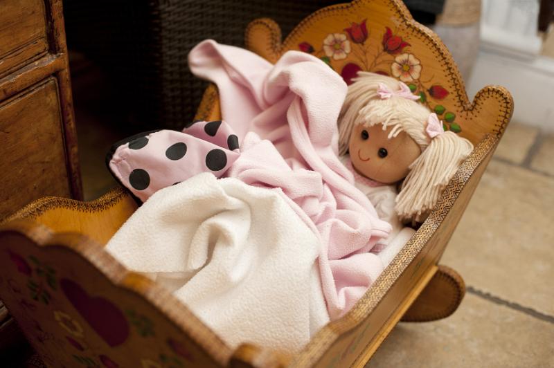 Free Stock Photo: Tight view of cute little blond doll wrapped in blankets laying down in wooden crib on floor