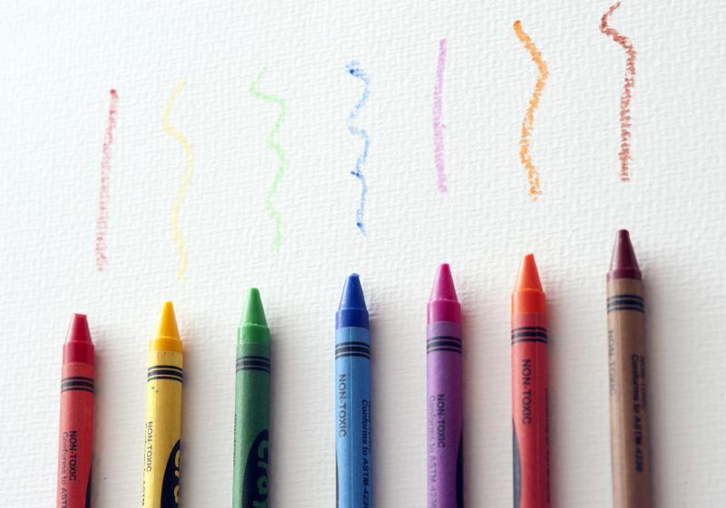 Free Stock Photo: Row of colored wax crayons with wavy squiggles drawn above in the colors of the rainbow, overhead on white