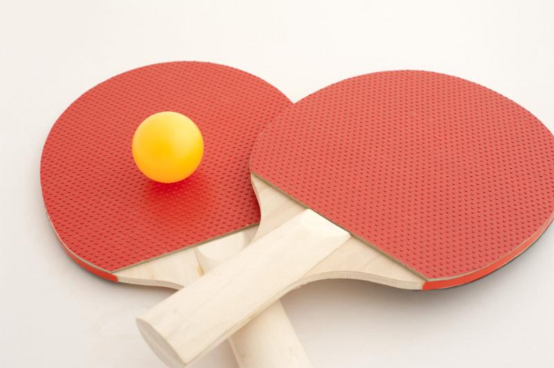 Free Stock Photo: Two wooden red ping pong bats with a yellow ball lying on an off white surface viewed low angle