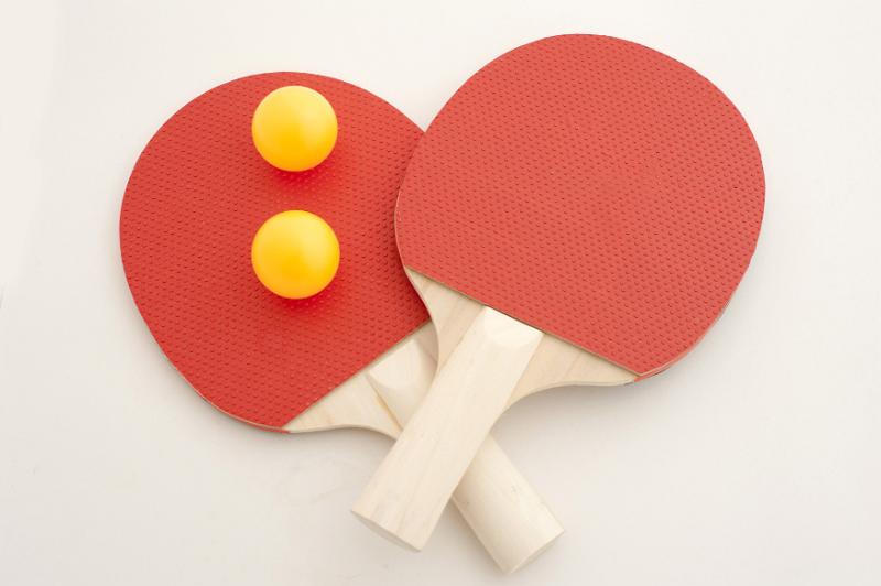 Free Stock Photo: Two red wooden ping pong or table tennis bats with luminous yellow balls crossing over on a white background viewed from above