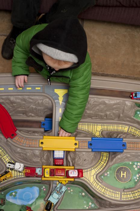 Free Stock Photo: Top down view of young child in green winter coat and black hood playing with vehicles on large toy train and road set