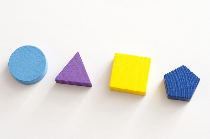 Free Stock Photo: Four different shaped wooden toy blocks laid out on a white background with a circle, triangle, square and pentagon