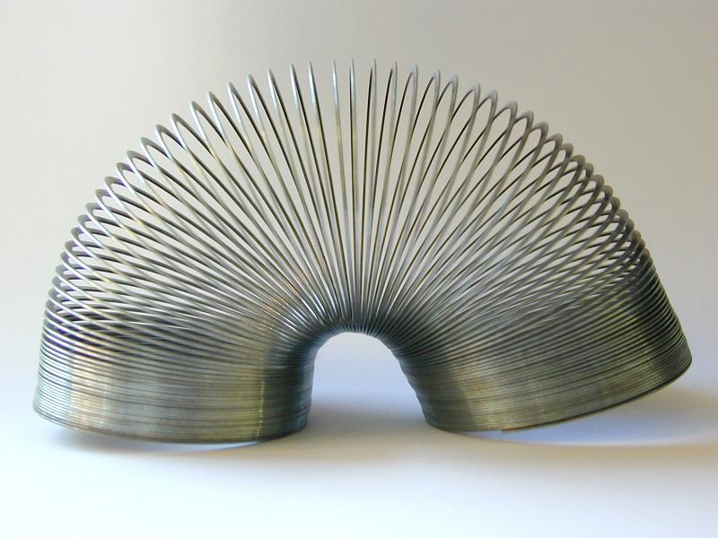 Free Stock Photo: Retro metal slinky toy famous for its perpetual looping arched over on a white studio background