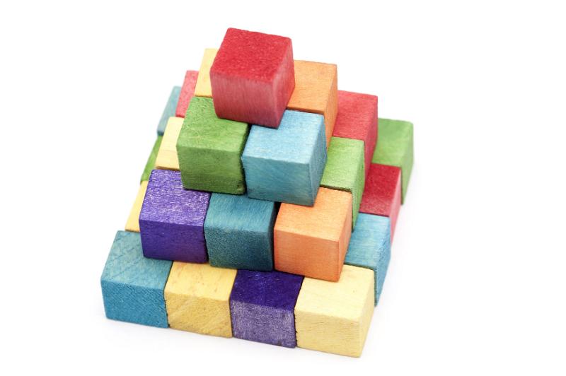 Free Stock Photo: Stacked colorful wooden kids toy bricks in the colors of the rainbow arranged in a pyramid on a white background, high angle view