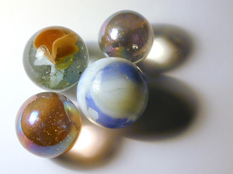 Free Stock Photo: Collection of four different childhood glass marbles casting creative shadows over a grey background with copy space