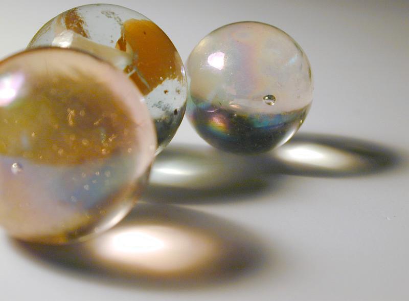 Free Stock Photo: Trio of toy glass marbles casting artistic ring form shadows over a grey background with copy space