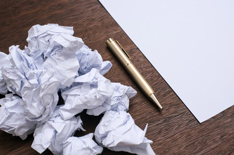 Free Stock Photo: Difficult work and writers block concept with a bunch of crumpled papers and a clean sheet with metal pen on the surface of wooden table, viewed in close-up