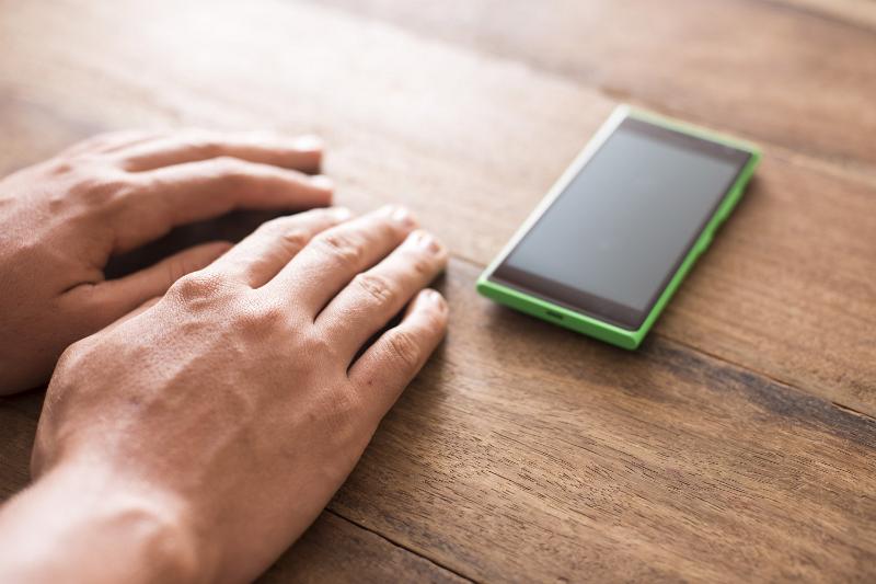 Free Stock Photo: Hands of a man resting on a wooden table alongside his mobile phone as he waits impatiently for a long-awaited call