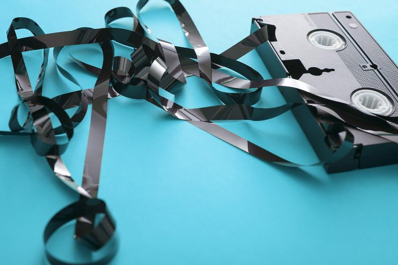 Free Stock Photo: In a mess concept with a tangled video tape pulled out of the cassette on a turquoise blue background with copy space