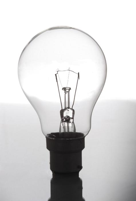 Free Stock Photo: Transparent glass incandescent light bulb balanced upright on a reflective surface in a power and energy concept