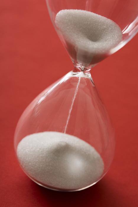 Free Stock Photo: Passing of precious time concept with a close up tilted view of sand running through an hour glass over a red background