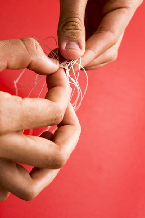 Free Stock Photo: Untangled concept with man unravelling a knot in fine twine with his fingers over a red background with copy space
