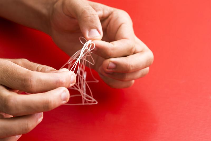 Free Stock Photo: Working on Problem concept with the hands of a man untangling a knot in fine twine over a red background with copy space