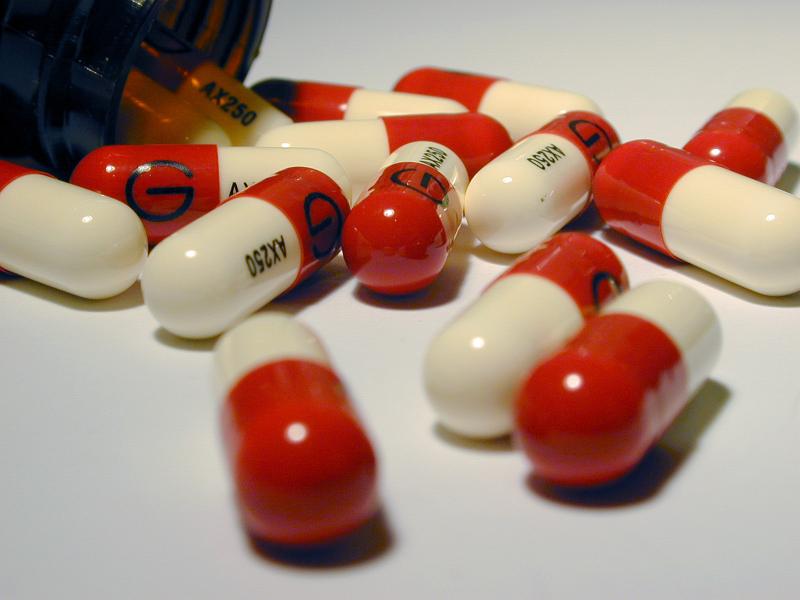 Free Stock Photo: Red and White Medication Capsules Spilled from Fallen Open Prescription Pill Bottle on White Background