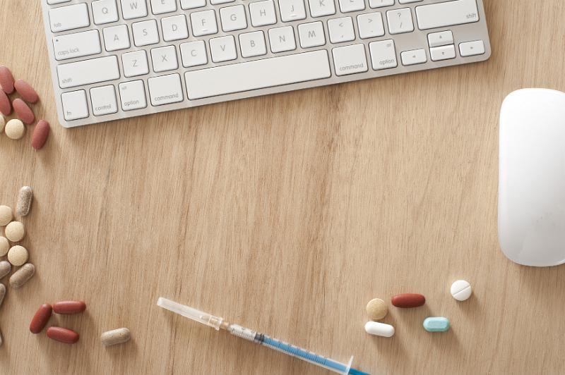 Free Stock Photo: Modern online medical concept with an overhead view of a computer keyboard and mouse with assorted tablets and a syringe on a wooden desk with copyspace