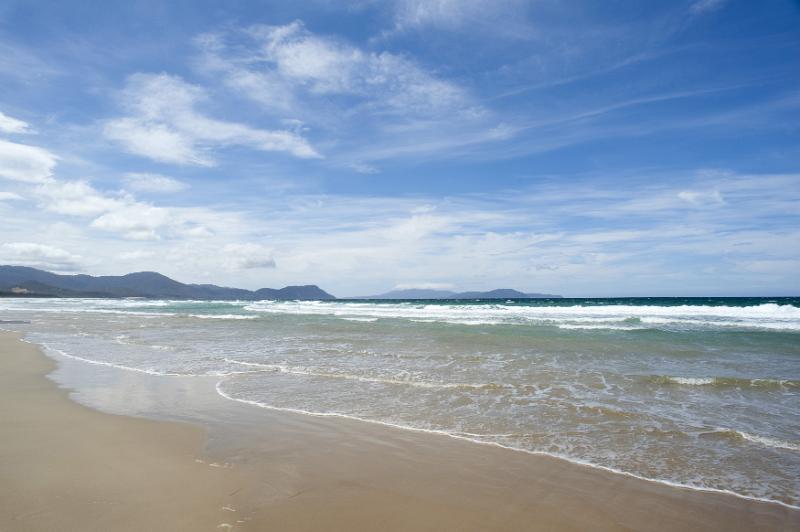 Free Stock Photo: Deserted scenic tropical beach with golden beach sand and waves breaking on the shore against a backdrop of distant mountains