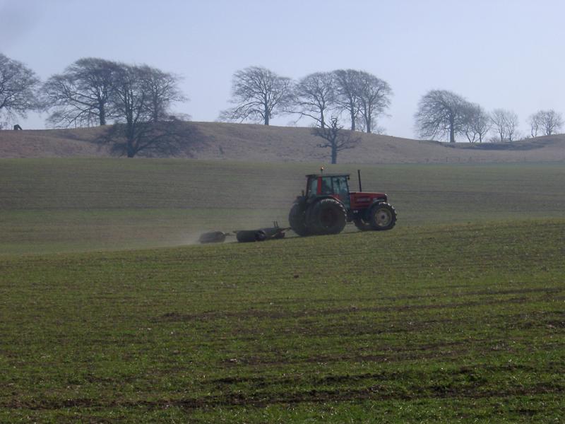 Free Stock Photo: Farmer working in the fields driving his tractor across a grassy field on a misty day with copyspace