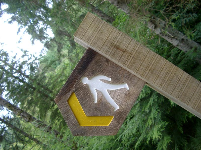 Free Stock Photo: Wooden sign marking a footpath showing a cutout of a walking man painted in white with a yellow arrow alongside in a woodland setting
