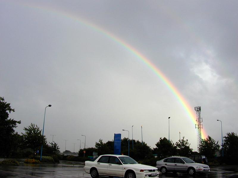 Free Stock Photo: Colorful Rainbow Arching Over Rain Soaked Parking Lot in Cloudy Sky in Aftermath of Rain Storm
