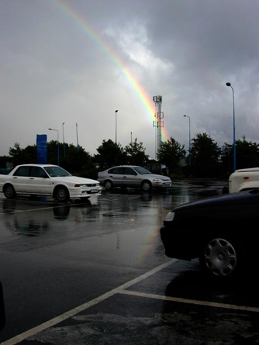 Free Stock Photo: Colorful rainbow on a rainy day viewed across a wet parking lot with cars breaking through stormy grey clouds