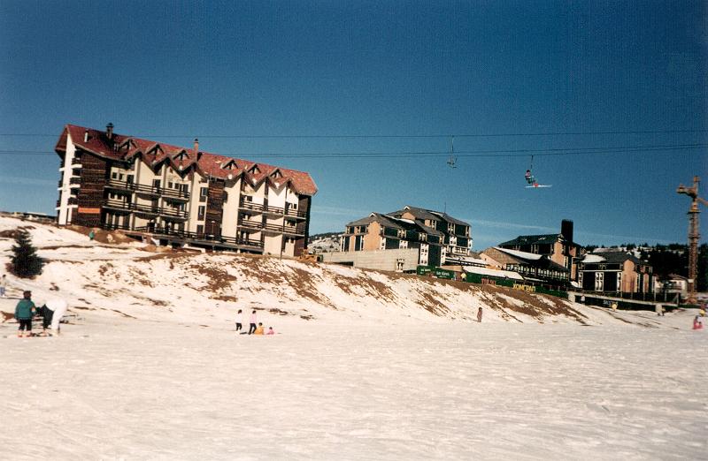 Free Stock Photo: Skiers at a winter resort on fresh white snow with a hotel or apartment block on the skyline and chalets in the distance